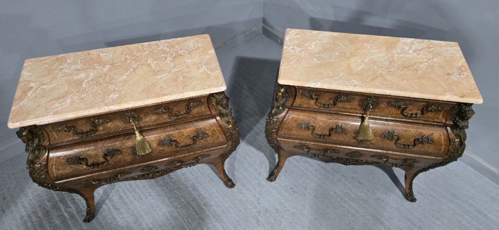 A pair of Louis XV style French bombe commodes featuring parquetry veneered drawer fronts, ornate metal mounts, and shaped marble tops. View II