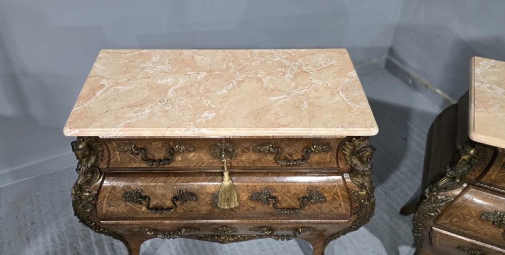 A pair of Louis XV style French bombe commodes featuring parquetry veneered drawer fronts, ornate metal mounts, and shaped marble tops. View III