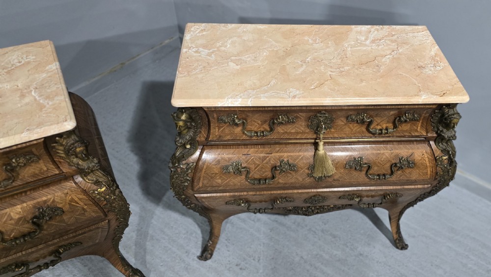 A pair of Louis XV style French bombe commodes featuring parquetry veneered drawer fronts, ornate metal mounts, and shaped marble tops. View V