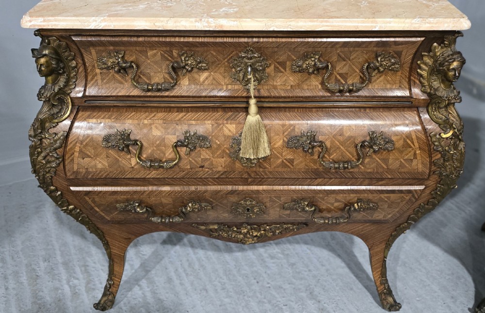 A pair of Louis XV style French bombe commodes featuring parquetry veneered drawer fronts, ornate metal mounts, and shaped marble tops. View VI