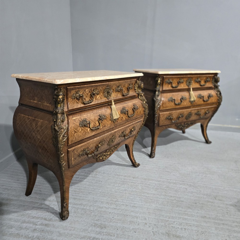 A pair of Louis XV style French bombe commodes featuring parquetry veneered drawer fronts, ornate metal mounts, and shaped marble tops. View XVII