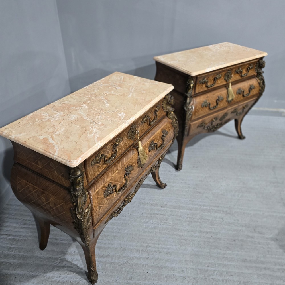 A pair of Louis XV style French bombe commodes featuring parquetry veneered drawer fronts, ornate metal mounts, and shaped marble tops. View XVIII