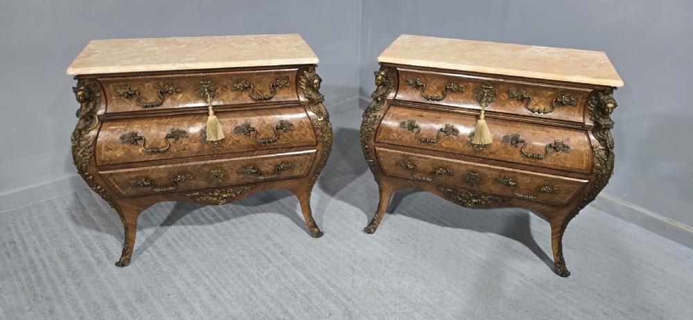 A pair of Louis XV style French bombe commodes featuring parquetry veneered drawer fronts, ornate metal mounts, and shaped marble tops. View XIX