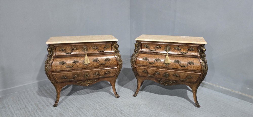 A pair of Louis XV style French bombe commodes featuring parquetry veneered drawer fronts, ornate metal mounts, and shaped marble tops. View XX