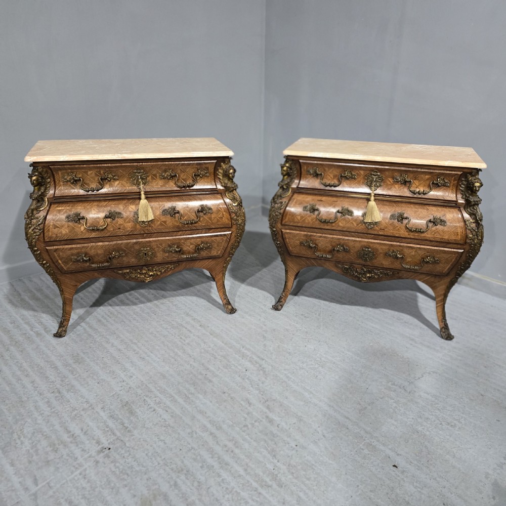 A pair of Louis XV style French bombe commodes featuring parquetry veneered drawer fronts, ornate metal mounts, and shaped marble tops. View XXI