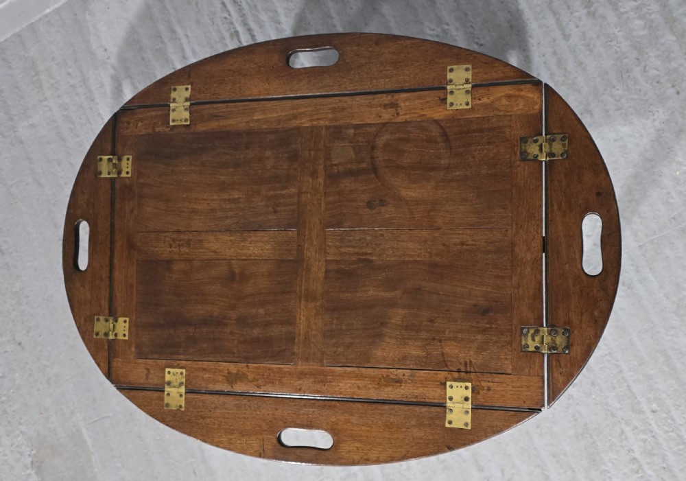 An oval Georgian mahogany butlers tray table featuring folding hinged sides with cutout handles on four straight legs. View V