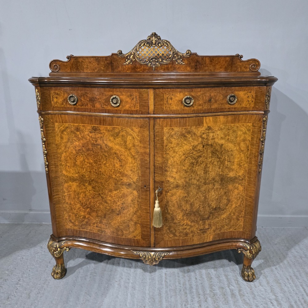 A Victorian burr walnut side cabinet featuring a serpentine front, carved upstand with pierced metal fretwork, ormolu mounts, and cabriole legs.