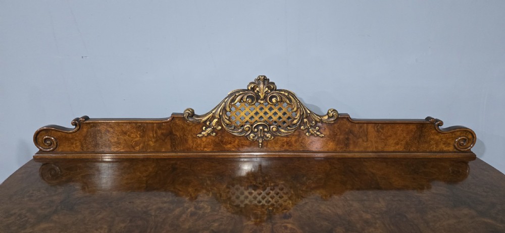 A Victorian burr walnut side cabinet featuring a serpentine front, carved upstand with pierced metal fretwork, ormolu mounts, and cabriole legs. View VI