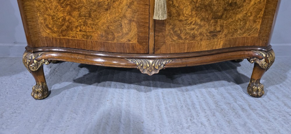 A Victorian burr walnut side cabinet featuring a serpentine front, carved upstand with pierced metal fretwork, ormolu mounts, and cabriole legs. View VII