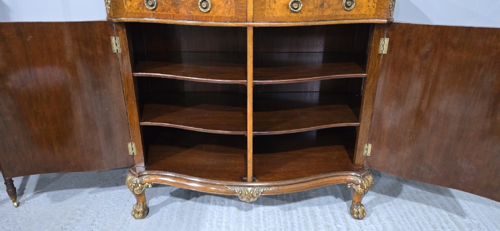 A Victorian burr walnut side cabinet featuring a serpentine front, carved upstand with pierced metal fretwork, ormolu mounts, and cabriole legs. View VIII