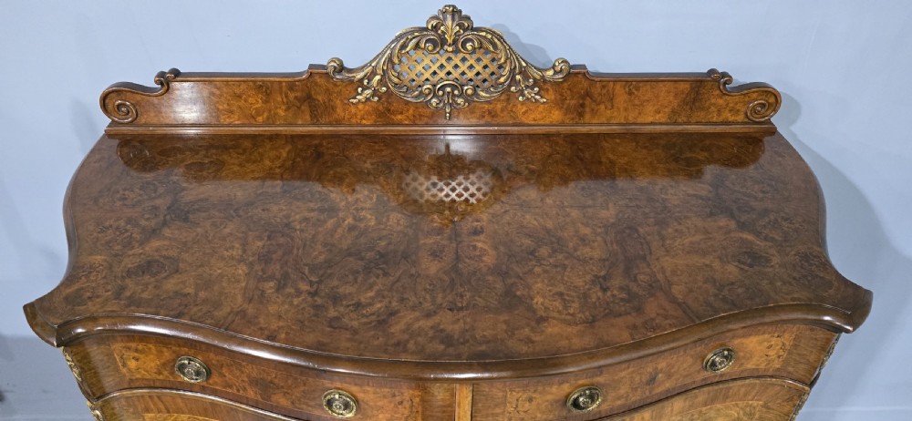 A Victorian burr walnut side cabinet featuring a serpentine front, carved upstand with pierced metal fretwork, ormolu mounts, and cabriole legs. View XIII