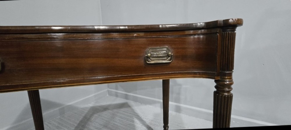 An antique Georgian mahogany side table featuring a single long drawer with brass handles and slender fluted tapered legs. View XI