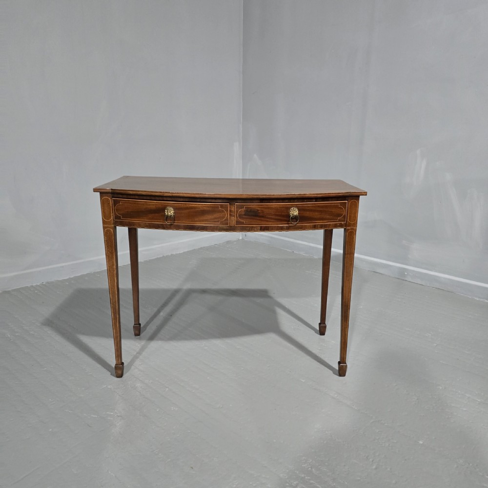 A Georgian mahogany bowfront side table featuring two string-inlaid drawers with lion mask brass handles, supported on square tapered legs.