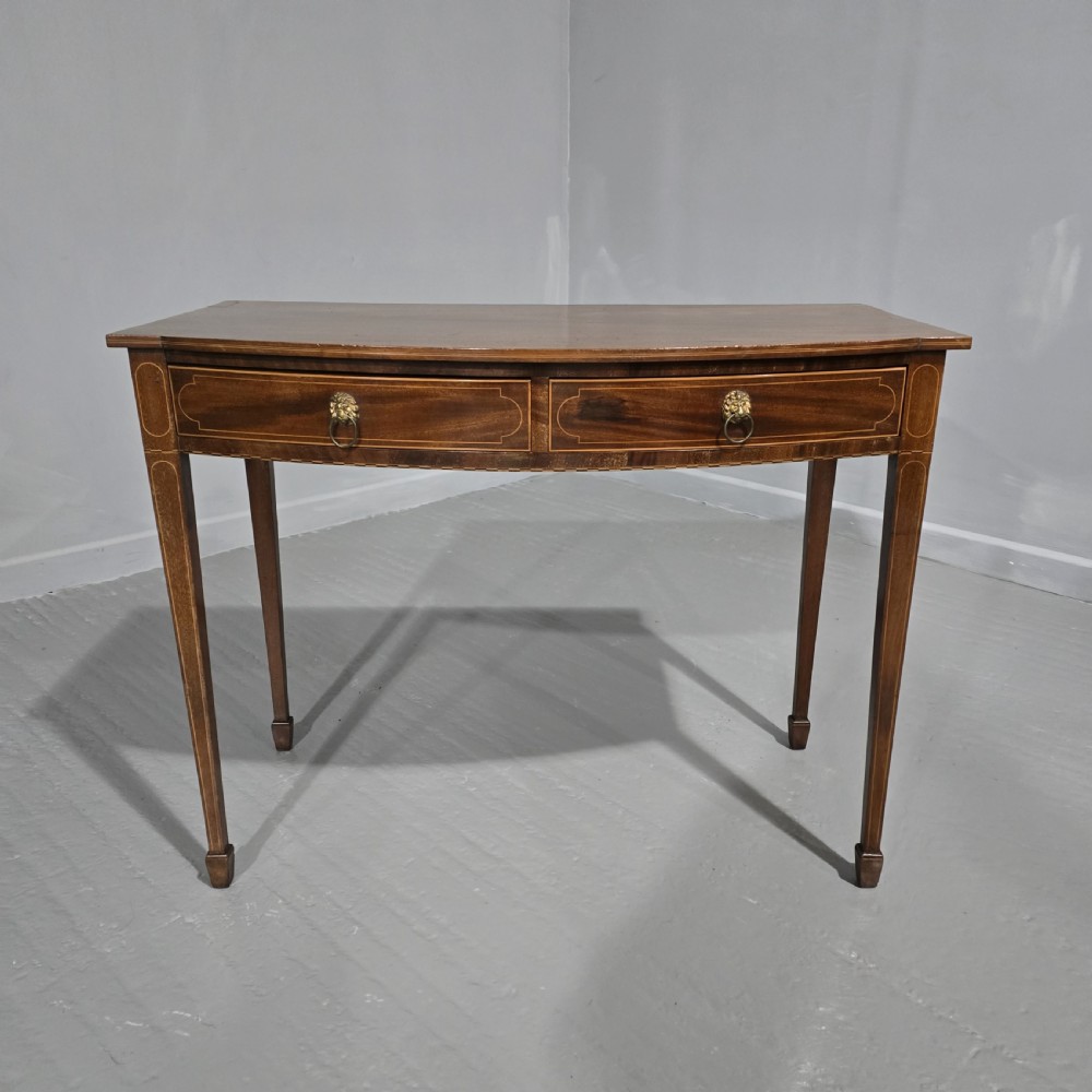 A Georgian mahogany bowfront side table featuring two string-inlaid drawers with lion mask brass handles, supported on square tapered legs. View II