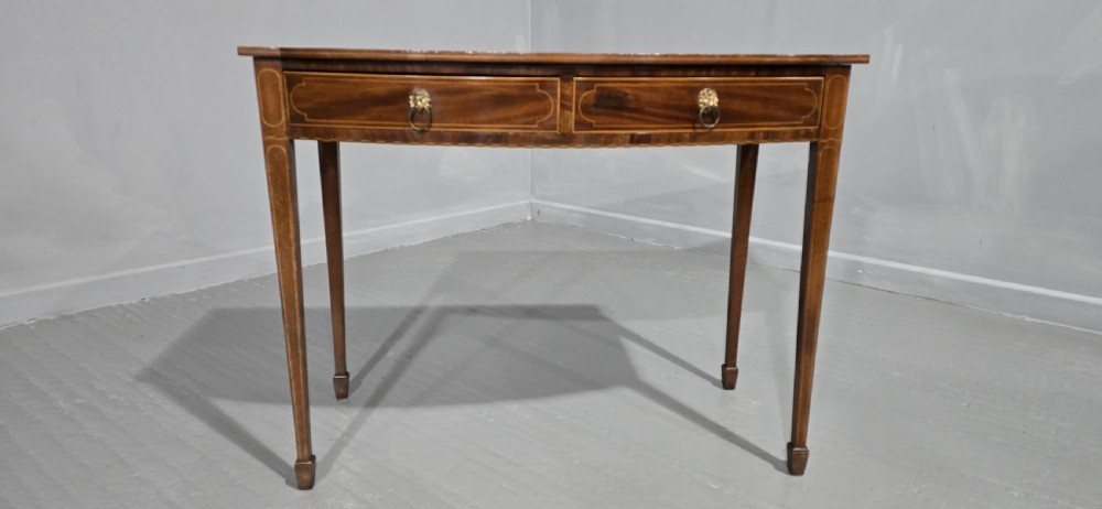 A Georgian mahogany bowfront side table featuring two string-inlaid drawers with lion mask brass handles, supported on square tapered legs. View III