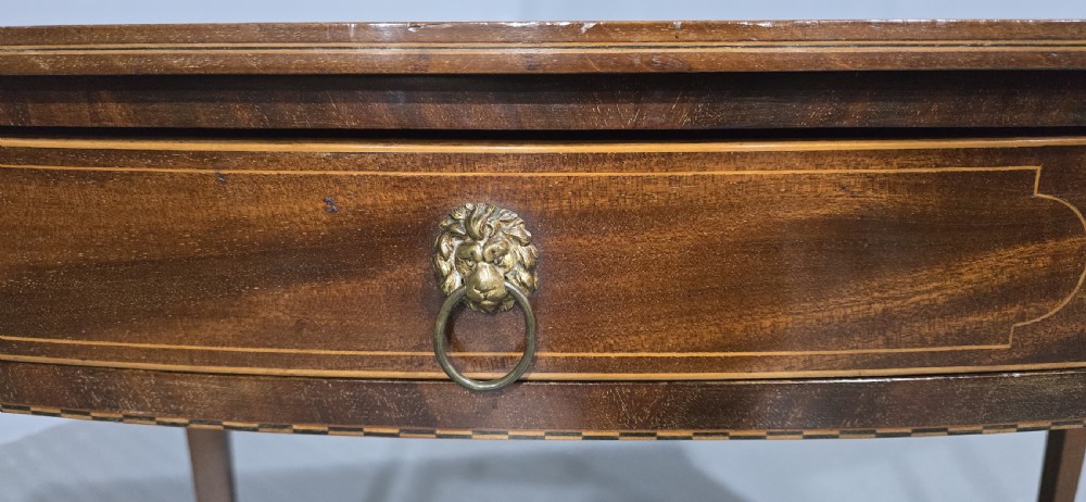 A Georgian mahogany bowfront side table featuring two string-inlaid drawers with lion mask brass handles, supported on square tapered legs. View VI