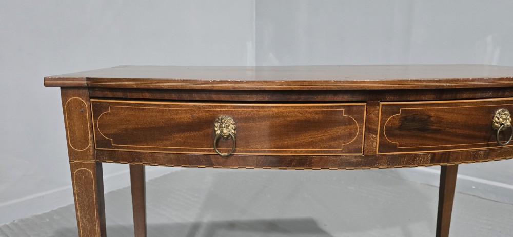 A Georgian mahogany bowfront side table featuring two string-inlaid drawers with lion mask brass handles, supported on square tapered legs. View VII