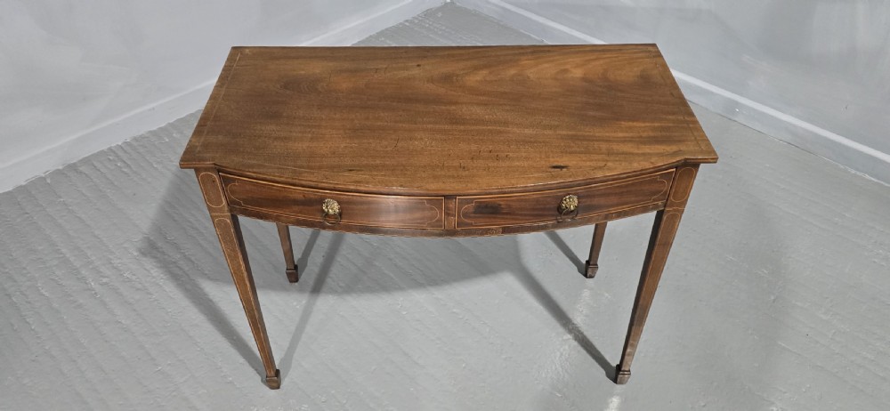 A Georgian mahogany bowfront side table featuring two string-inlaid drawers with lion mask brass handles, supported on square tapered legs. View IX