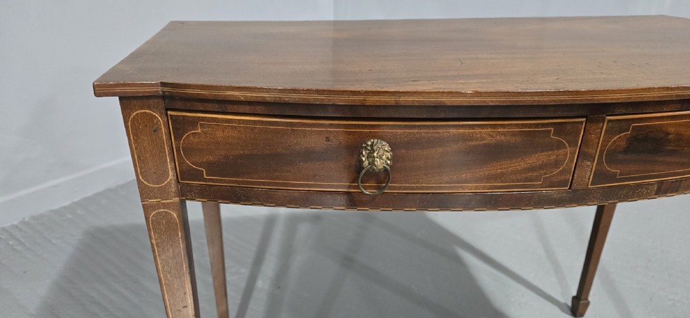 A Georgian mahogany bowfront side table featuring two string-inlaid drawers with lion mask brass handles, supported on square tapered legs. View XIII