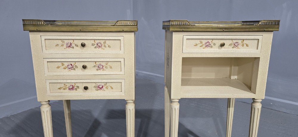 A pair of cream painted French bedside tables featuring brass gallery edges, marble inset tops, hand-painted floral drawer details, and slender fluted tapered legs. View III
