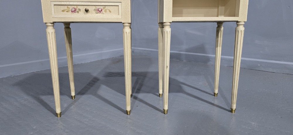 A pair of cream painted French bedside tables featuring brass gallery edges, marble inset tops, hand-painted floral drawer details, and slender fluted tapered legs. View V