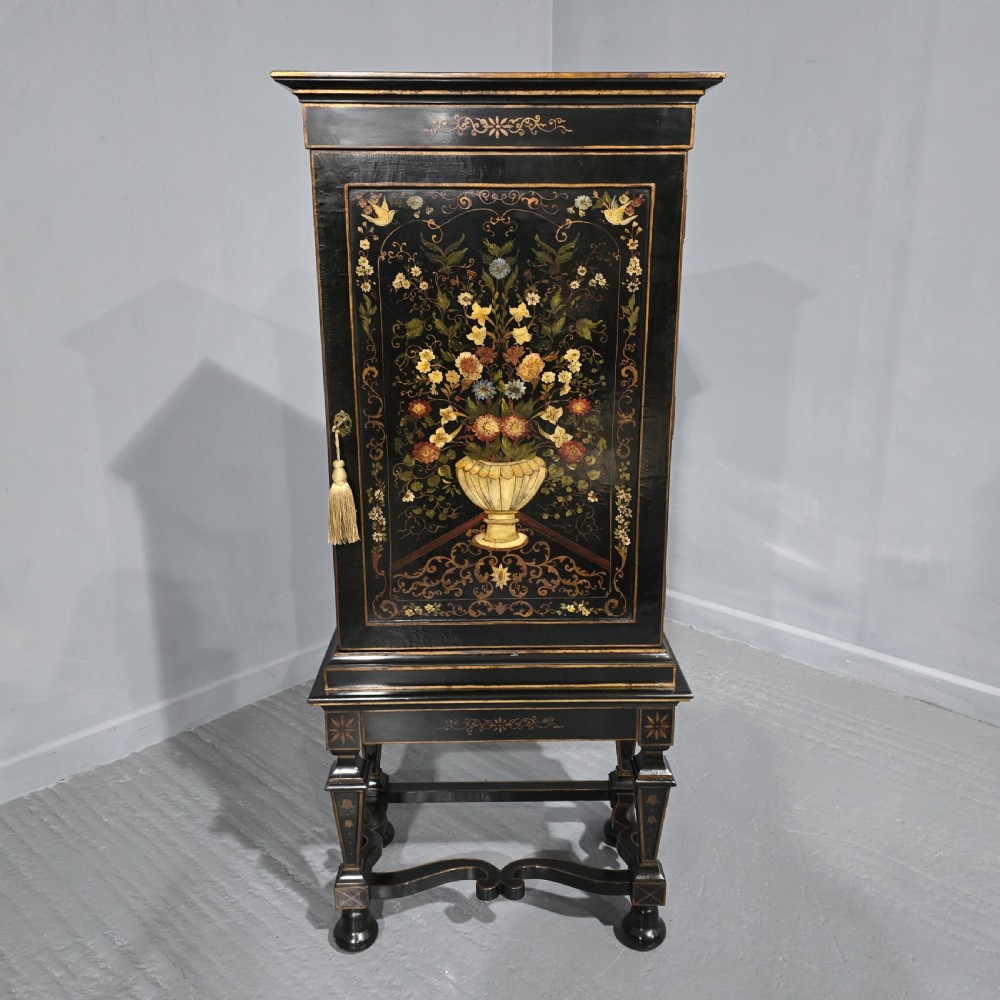 A tall black lacquered cabinet on stand featuring hand-painted floral urn artwork on the front door and curved stretchered legs.