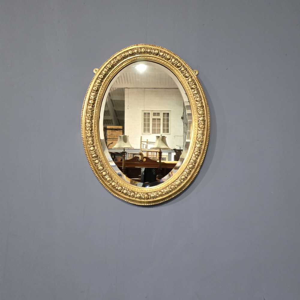 A Victorian oval wall mirror featuring a gilt gesso frame decorated with egg-and-dart moulding and a bevelled glass plate.