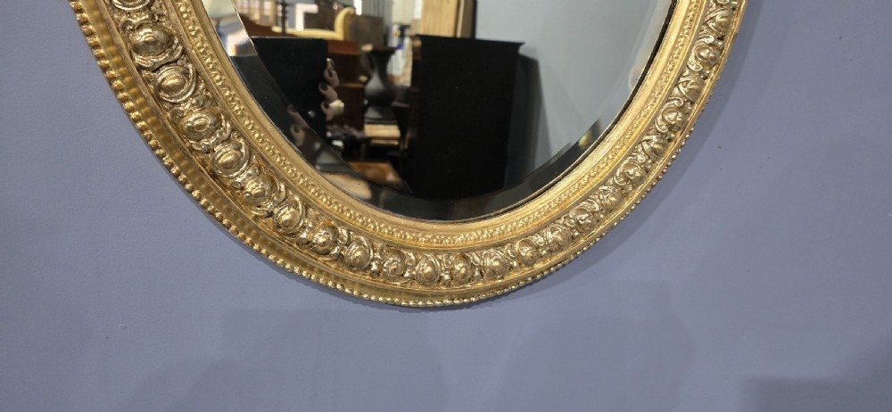 A Victorian oval wall mirror featuring a gilt gesso frame decorated with egg-and-dart moulding and a bevelled glass plate. View IV