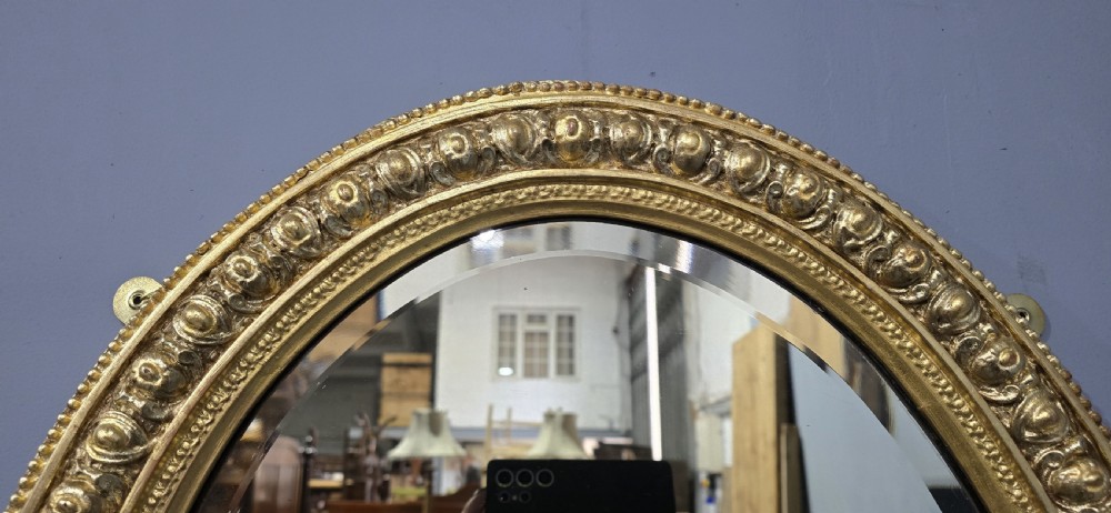 A Victorian oval wall mirror featuring a gilt gesso frame decorated with egg-and-dart moulding and a bevelled glass plate. View VII