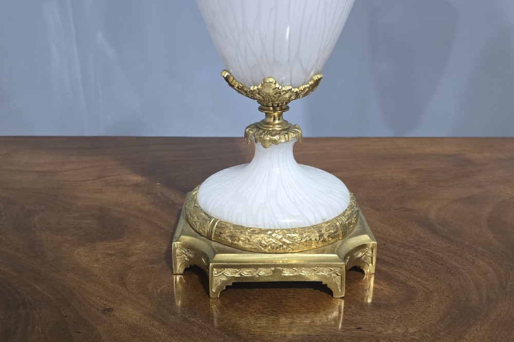 An antique French table lamp with an urn-shaped white opaline glass body, chased gilt bronze ormolu mounts, and a cream flared fabric shade. View II