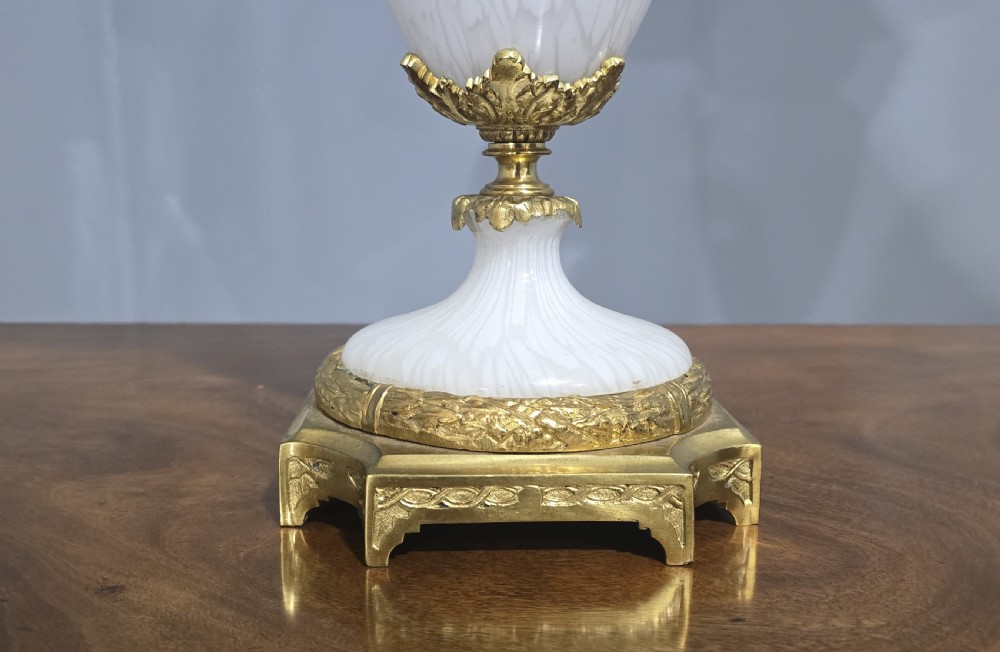 An antique French table lamp with an urn-shaped white opaline glass body, chased gilt bronze ormolu mounts, and a cream flared fabric shade. View IV