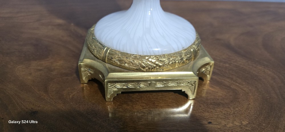 An antique French table lamp with an urn-shaped white opaline glass body, chased gilt bronze ormolu mounts, and a cream flared fabric shade. View VII