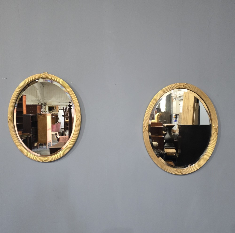 A pair of Victorian oval wall mirrors with reeded gilt frames featuring crossed ribbon motifs at four points and bevelled glass plates.