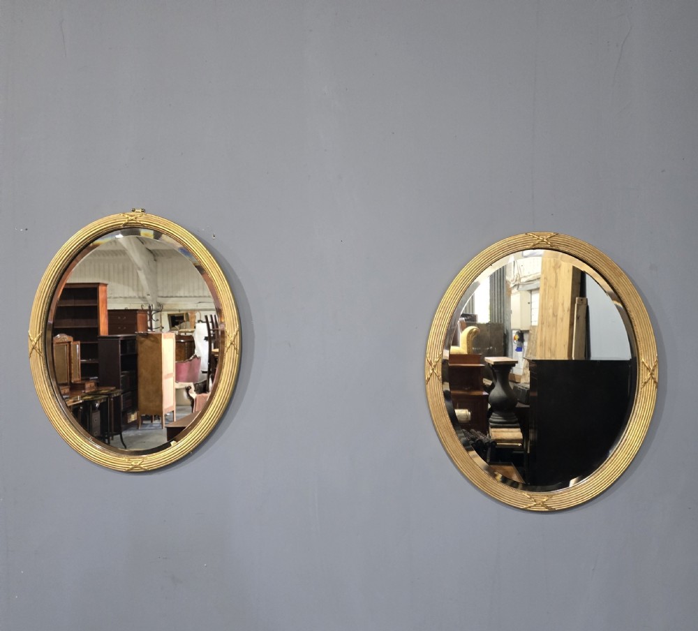 A pair of Victorian oval wall mirrors with reeded gilt frames featuring crossed ribbon motifs at four points and bevelled glass plates. View II