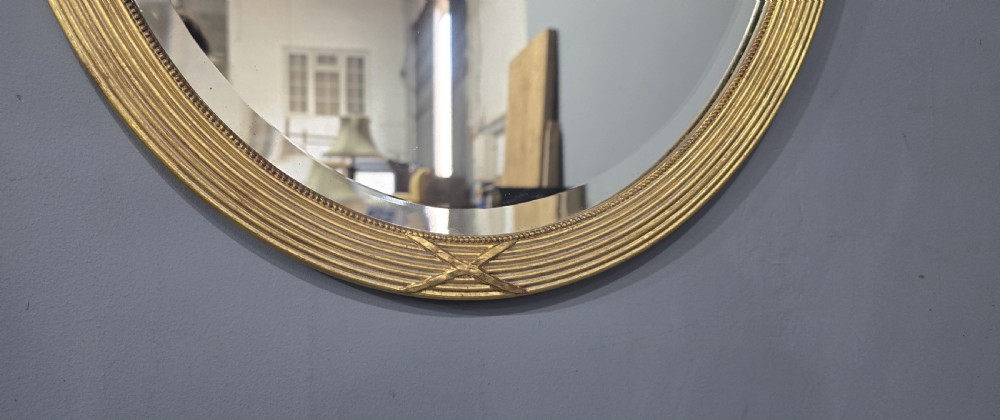A pair of Victorian oval wall mirrors with reeded gilt frames featuring crossed ribbon motifs at four points and bevelled glass plates. View IX