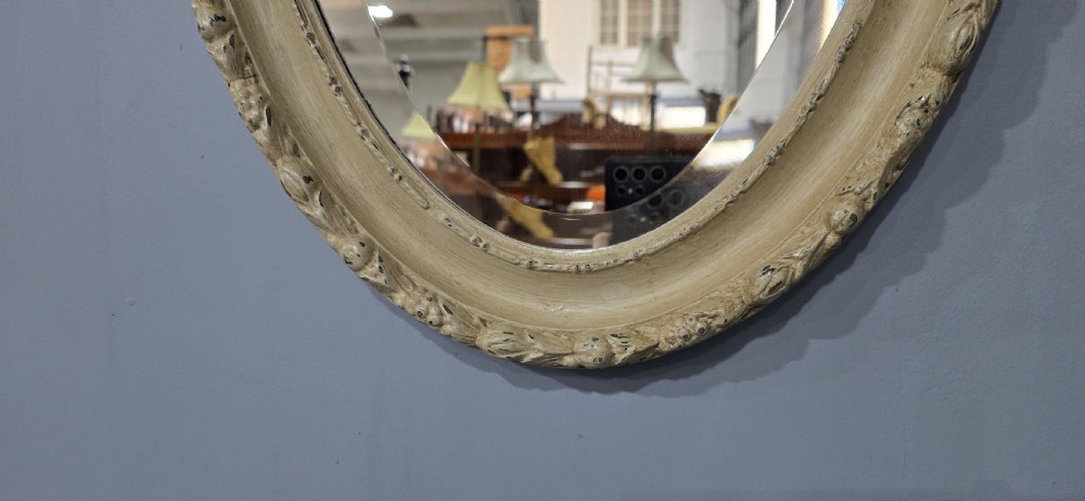 An oval Victorian wall mirror featuring a painted off-white frame with moulded foliage details around the border. View III