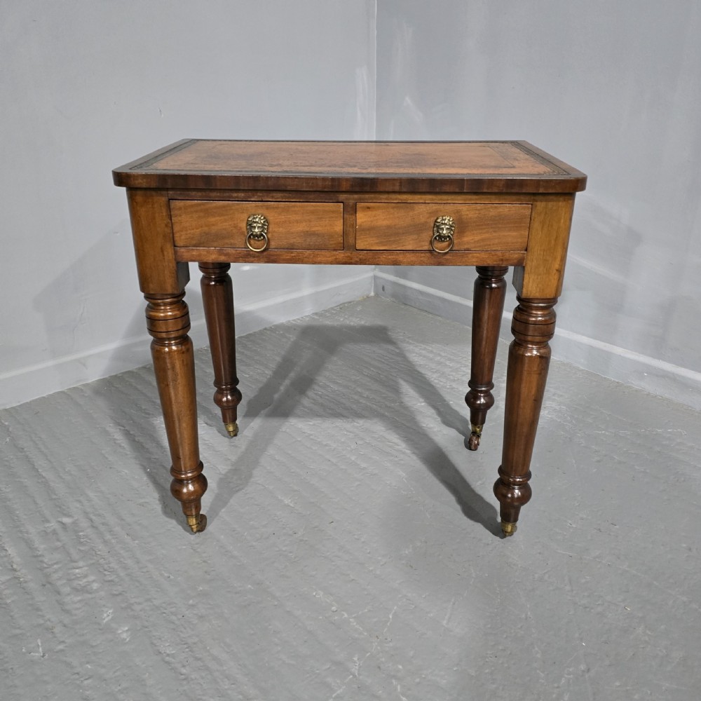 A small Victorian mahogany writing desk featuring a leather-inset top, two frieze drawers with brass lion-head ring handles, and turned legs on brass castors.