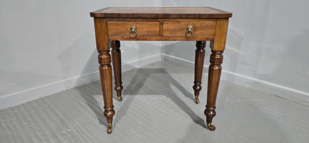 A small Victorian mahogany writing desk featuring a leather-inset top, two frieze drawers with brass lion-head ring handles, and turned legs on brass castors. View II