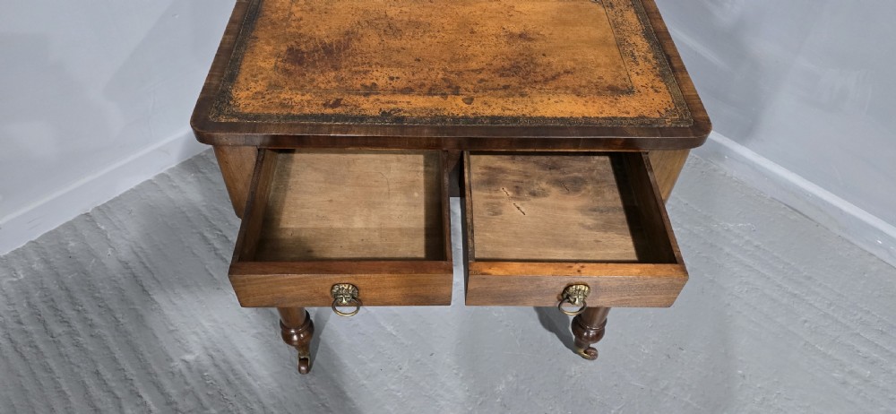 A small Victorian mahogany writing desk featuring a leather-inset top, two frieze drawers with brass lion-head ring handles, and turned legs on brass castors. View IV