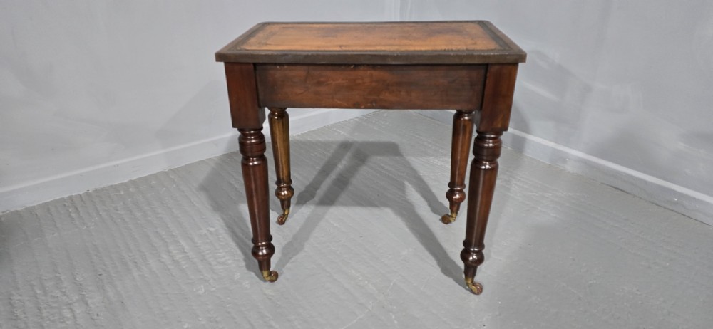 A small Victorian mahogany writing desk featuring a leather-inset top, two frieze drawers with brass lion-head ring handles, and turned legs on brass castors. View VI