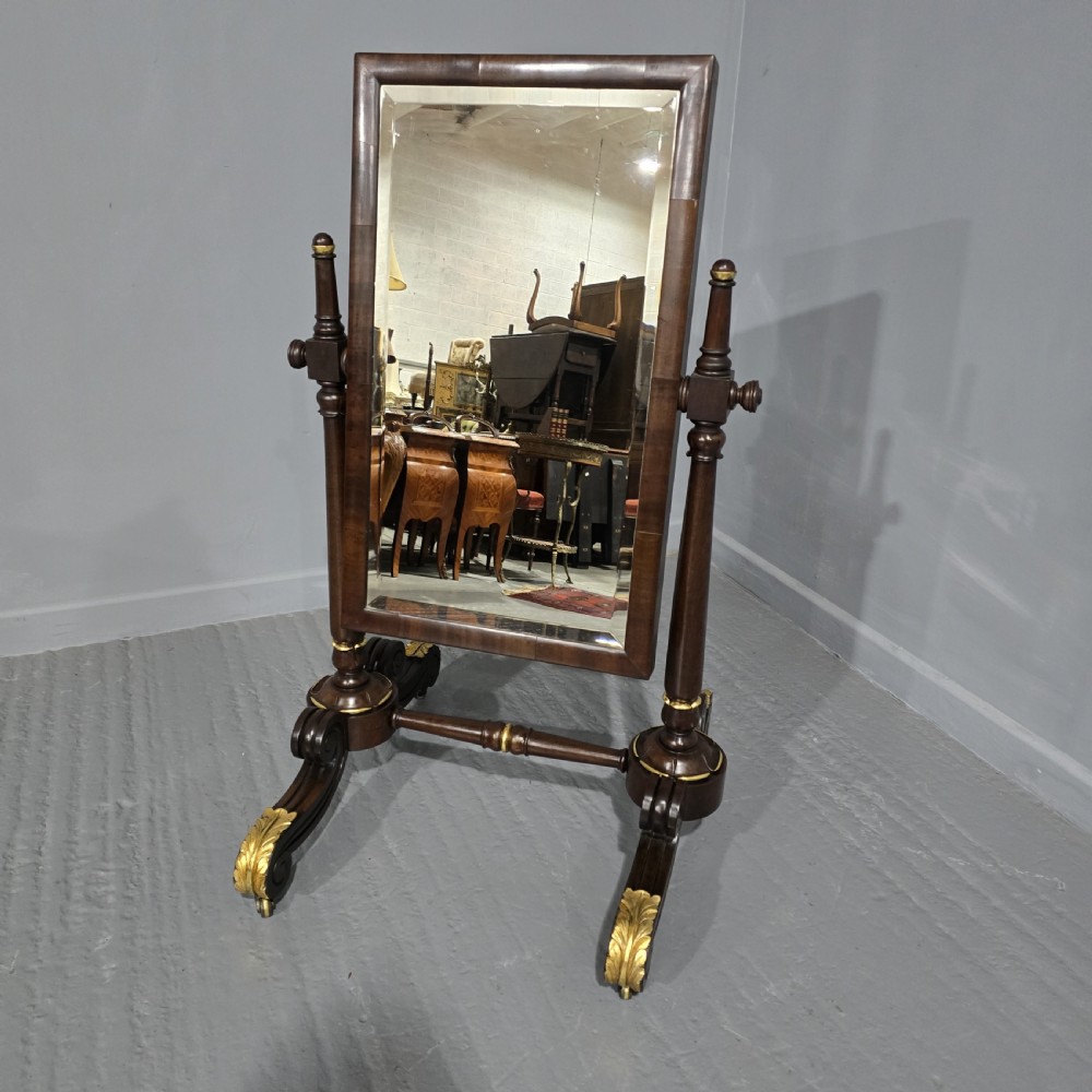 A Regency mahogany cheval mirror featuring a rectangular tilting glass frame supported by turned upright posts and splayed legs with gilded leaf ornamentation.