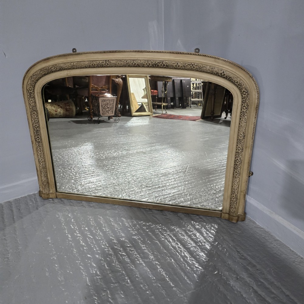 A Victorian arched overmantel mirror with a cream painted wooden frame detailed with floral relief moulding.