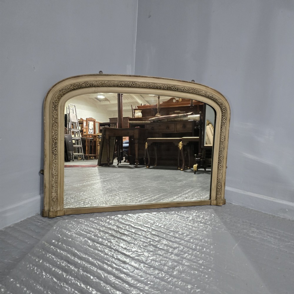 A Victorian arched overmantel mirror with a cream painted wooden frame detailed with floral relief moulding. View II