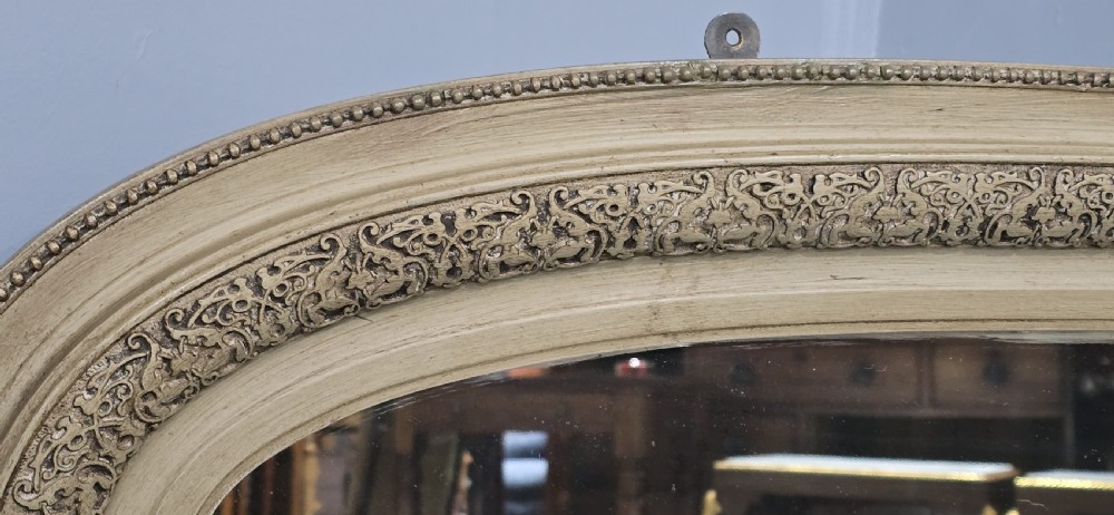 A Victorian arched overmantel mirror with a cream painted wooden frame detailed with floral relief moulding. View IV