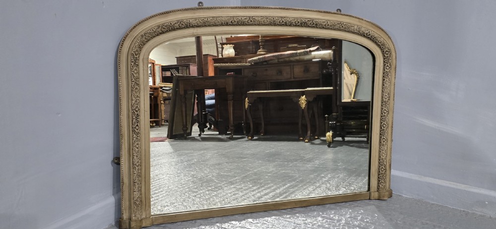 A Victorian arched overmantel mirror with a cream painted wooden frame detailed with floral relief moulding. View VI