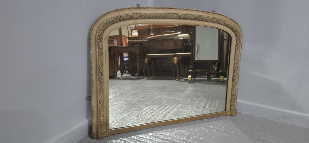 A Victorian arched overmantel mirror with a cream painted wooden frame detailed with floral relief moulding. View VIII
