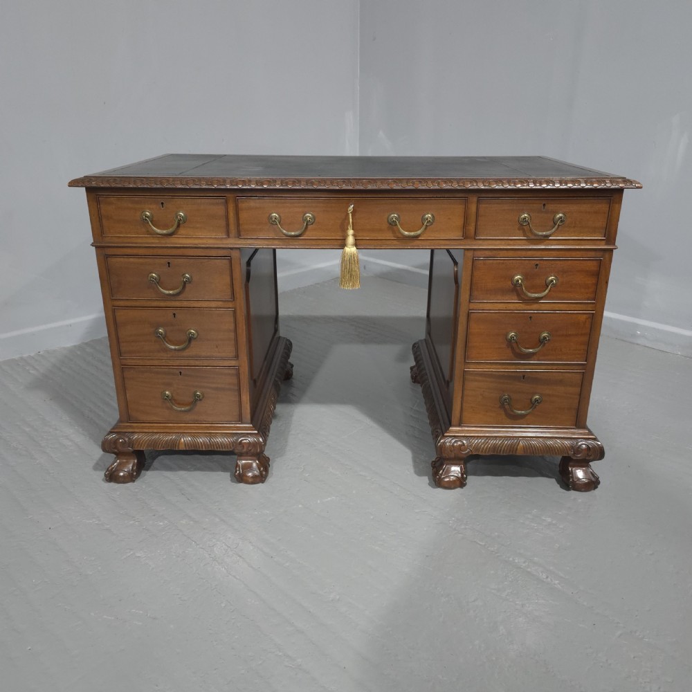An antique mahogany pedestal desk featuring a dark leather inset surface, brass swan-neck handles, eight side drawers, a central frieze drawer, and carved claw feet.