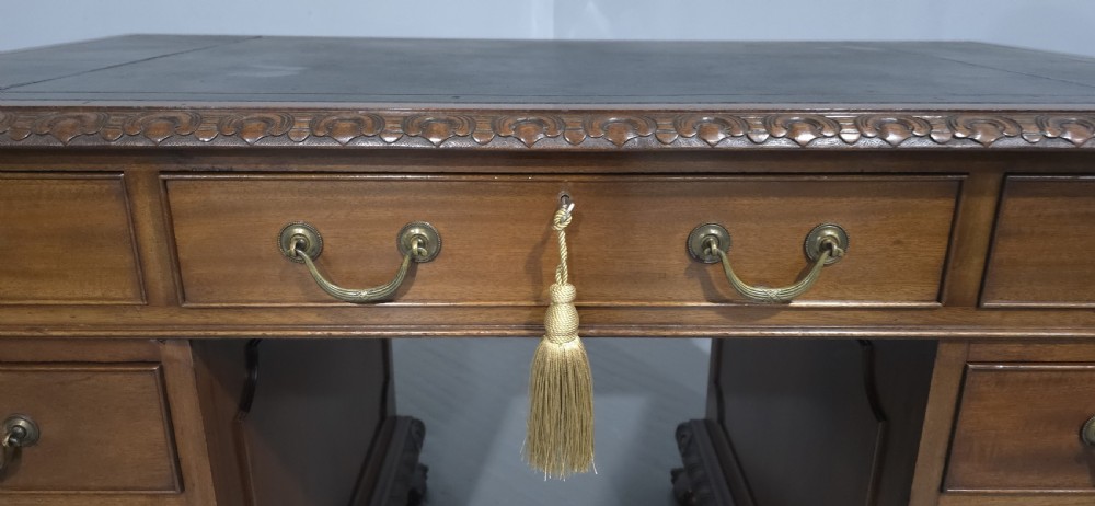 An antique mahogany pedestal desk featuring a dark leather inset surface, brass swan-neck handles, eight side drawers, a central frieze drawer, and carved claw feet. View III