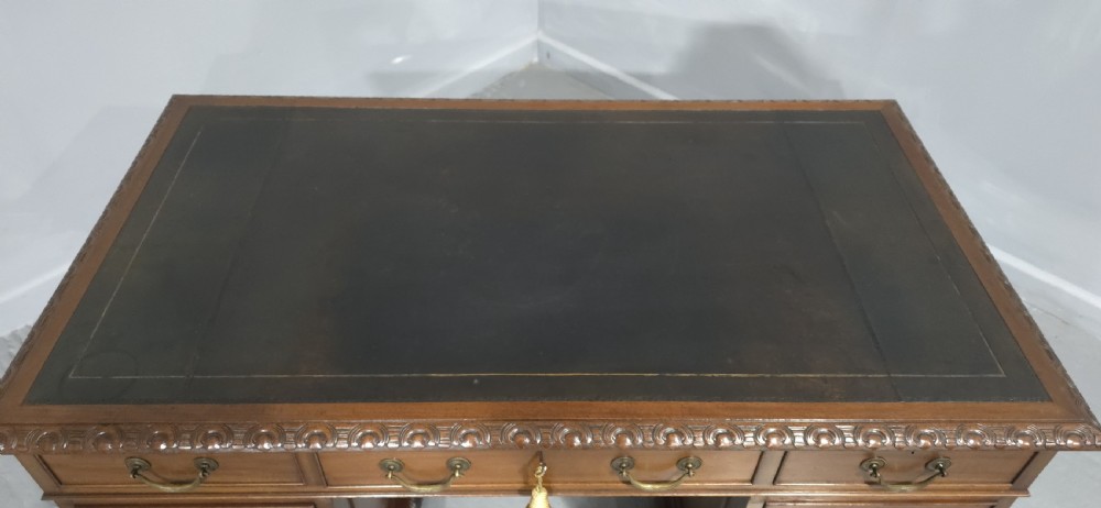 An antique mahogany pedestal desk featuring a dark leather inset surface, brass swan-neck handles, eight side drawers, a central frieze drawer, and carved claw feet. View V