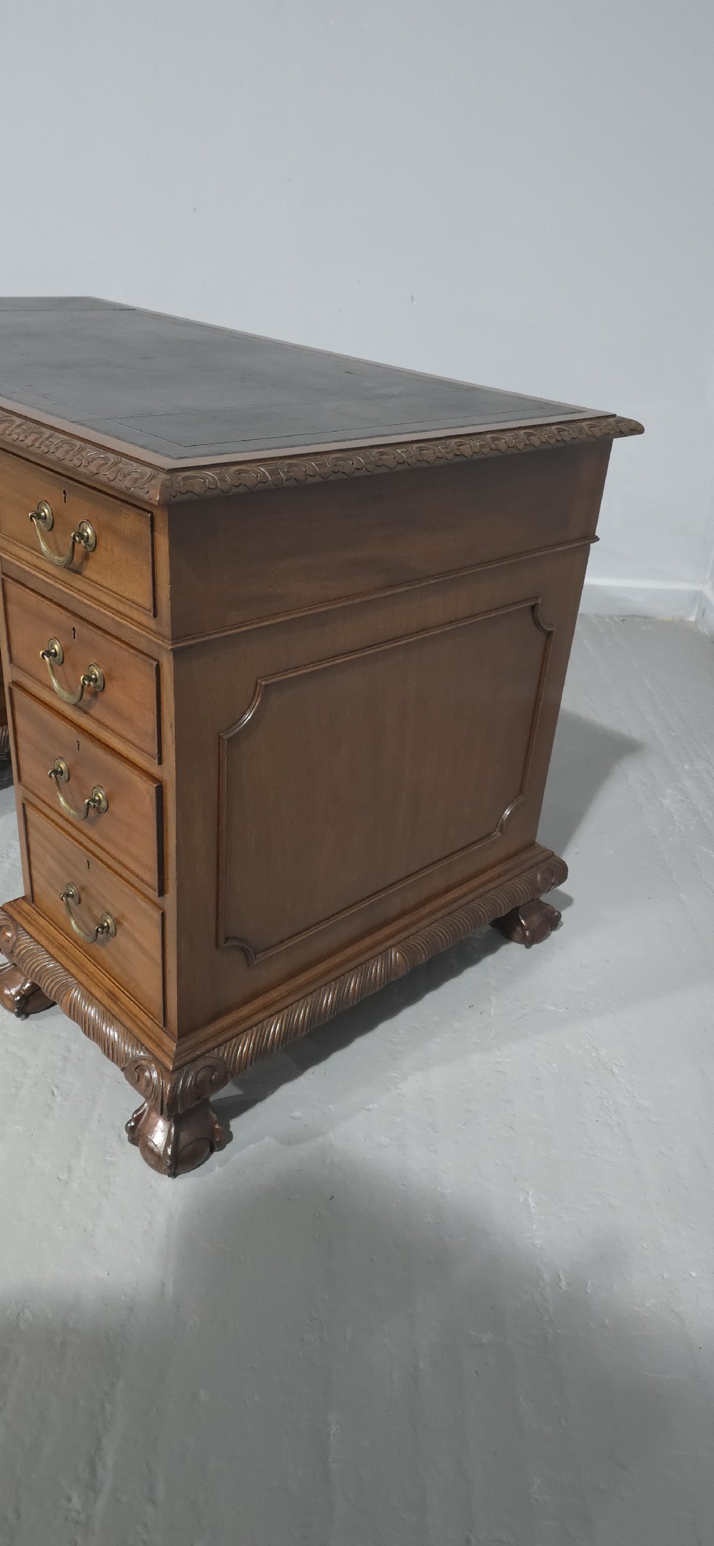 An antique mahogany pedestal desk featuring a dark leather inset surface, brass swan-neck handles, eight side drawers, a central frieze drawer, and carved claw feet. View X
